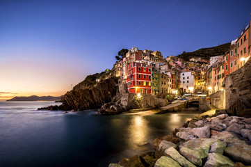 Fototapeta na wymiar Riomaggiore fisherman village at sunset. Riomaggiore is one of five famous colorful villages of Cinque Terre in Italy, suspended between sea and land on sheer cliffs. Liguria, Italy