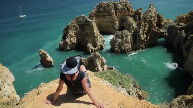Tourism in Algarve. Summer holidays in Portugal, Europe. Lifestyle tourist sitting on promontory of Ponta da Piedade. Caucasian woman looking amazing views of iconic cliffs of turquoise sea of Lagos.