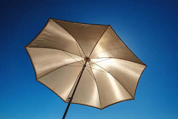 The beach umbrella protects from the bright sun, bottom view. Yellow sun protector under blue sky - summer vacation background