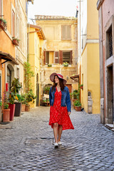 Happy woman in dress and hat walking on paved old street of Rome looking happily around.