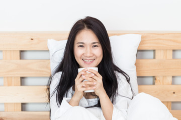 Beauty Asian woman smile and holding coffee cup on her bed in the morning
