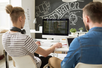 Rear view of concentrated coders using computer and analyzing computer program script while working...