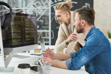 Positive program writers discussing computer language code while making web script on computer and discussing project in modern office
