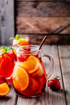 Homemade red wine sangria with orange, apple, strawberry and ice in pitcher  and glass on wooden background