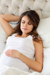 A beautiful pregnant woman sleeps in a white bed. Conception of pregnancy, motherhood.