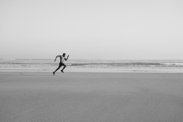 Black man running by the sea on the beach. Powerful runner sprinting and training on summer.