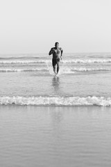 Fototapeta na wymiar Fit black man running at seaside splashing watter. Black runner training legs power sprinting at the beach. Summer healthy lifestyle and sport motivation concept.