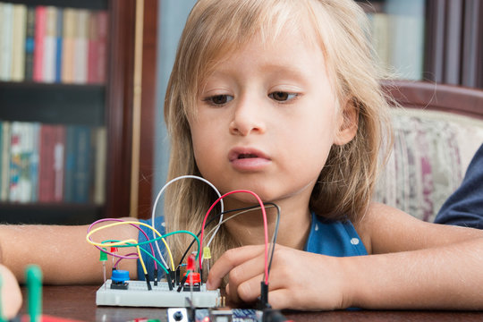 A cute girl with a teacher collect robot arduino and program it on the computer. The boards and microcontrollers are on the table. STEM education. Programming. Mathematics. The science. Technologie.