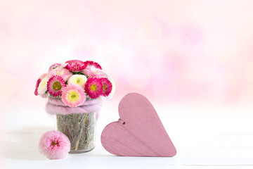 Bellis in Glasgefäß und Herz als Gruß zum Muttertag