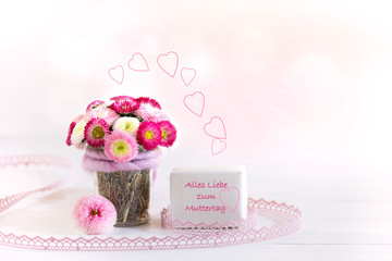 Bellis in Glasgefäß vor hellem Hintergrund mit Gruß zum Muttertag