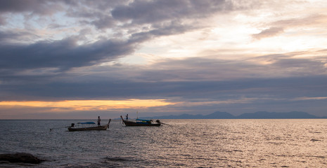 Colorful seascape with traditional thai boats with fishermen at evening fishing, scenic clouds and shadowy mountains in skyline. Andaman sea, Ao Nang, Krabi province, Thailand.