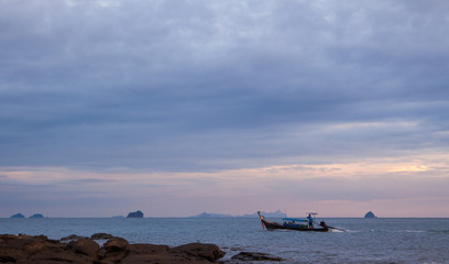 Colorful seascape with lonely traditional thai boat, scenic clouds and shadowy islands in skyline....