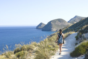  young woman with backpack walking on a path near the sea