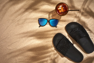 Sandal and sunglasses on a sandy background, top view