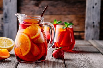 Homemade red wine sangria with orange, apple, strawberry and ice in pitcher and glass on wooden background
