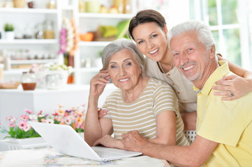 happy senior couple with adult daughter using laptop 