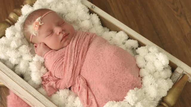 Two-weeks old newborn baby girl sleeping in a little wooden bowl