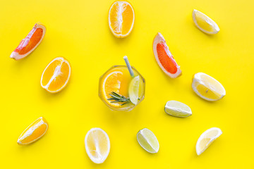Concept of alcoholic cocktail with fruits. Glass with beverage near oranges, grapefruit, lime and rosemary on yellow background top view pattern