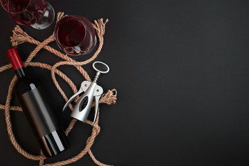Red wine bottle, two glasses and corkscrew on black background. Top view with copy space
