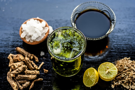 Sharbat or Indian styled water beverage of Nannari or Indian sarsaparilla with all its ingredients i.e. Nannari syrup,water,ice cubes, lemon juice and sweet basil on wooden surface.