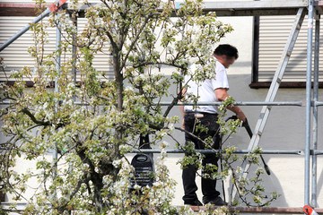 Robotnik, malarz myje karcherem ścianę, fasade budynku mieszkalnego stojąc na rusztowaniu.