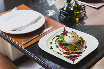 Burrata cheese salad including sliced tomato, onion, grape, basil leaves with pesto sauce and red sauce.