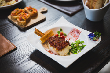 Baked Cod fish with sauce, pan grilled baby vegetables, pea and tomato served with bread sticks.