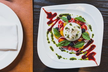 Burrata cheese salad including sliced tomato, onion, grape, basil leaves with pesto sauce and red sauce.