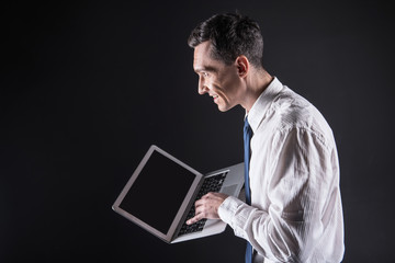 Pleasurable experience. Happy positive nice man holding a laptop and looking at the computer screen while being in a great mood