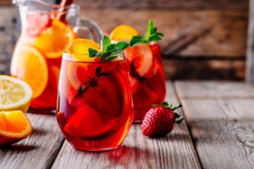 Homemade red wine sangria with orange, apple, strawberry and ice in glass and pitcher on wooden background.