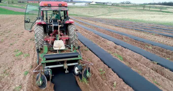 Extreme aerial closeup of tractor laying plastic mulch on a farm.