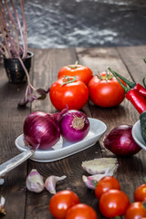 Tomatoes, cucumbers, onions, radish, garlic, pepper, dill, garlic and mushrooms on a dark wooden background.