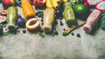 Flat-lay of colorful smoothies in bottles with fresh tropical fruit and superfoods on concrete background, top view, copy space. Healthy, vegetarian, detox, dieting breakfast food concept