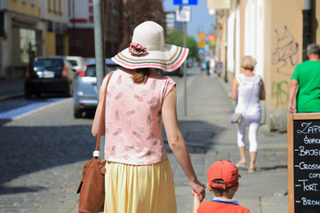 Kobieta w kapeluszu na spacerze z synem w mieście od tyłu.