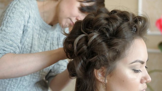 Makeup artist stylist works with model. hairdresser does the hair styling of the model. woman is working a styler with the girl's long hair. The hairdresser makes curls on the girl's straight hair.