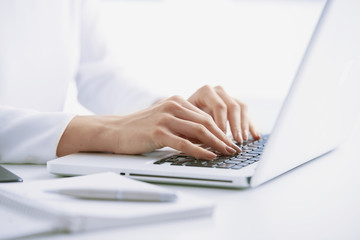 Typing on laptop keyboard. Close-up of a young woman holding brush in her hand and applying makeup. Isolated on light blue background.