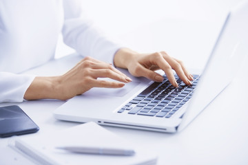 Obraz na płótnie Canvas Typing on laptop keyboard. Close-up of a young woman holding brush in her hand and applying makeup. Isolated on light blue background.