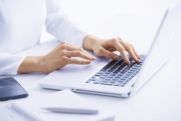 Typing on laptop keyboard. Close-up of a young woman holding brush in her hand and applying makeup. Isolated on light blue background.