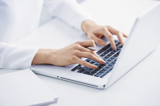 Typing on laptop keyboard. Close-up of a young woman holding brush in her hand and applying makeup. Isolated on light blue background.