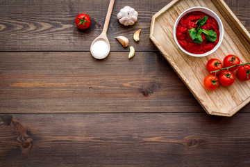 Homemade tomato ketchup with cherry tomatoes, garlic and basil on dark wooden background top view space for text