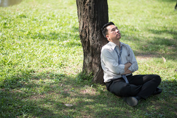 Business man failing and serious under tree in the park. He is stressed with work Unsuccessful disappointed in project