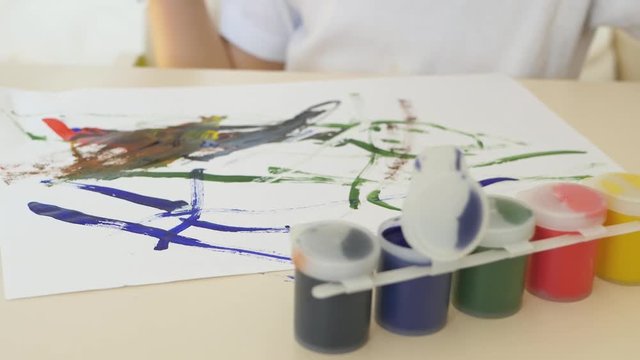 Hands of the child draws watercolor drawings on a white sheet of paper sitting at the table. Close-up. The motion camera slider.