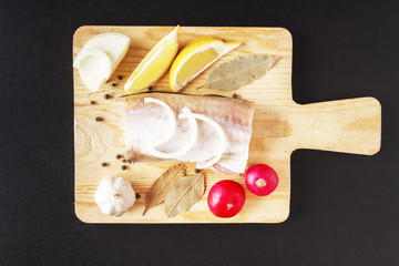 Uncooked ingredients for healthy food from sea fish with vegetables and seasoning on wooden board. Top view over black background