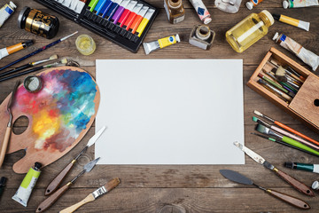 Set of artist accessories collection. Canvas, tube of oil paint, art brushes, palette knife lying on the wood table. Artist workshop background. - obrazy, fototapety, plakaty