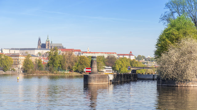 The lighthouse, navigation or orientation landmark and the lock, gate built on the riverbank of one of Prague island Zofin. The cityscape of Prague Castle in the background of image.