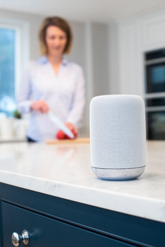 Woman Working In Kitchen With Smart Speaker In Foreground
