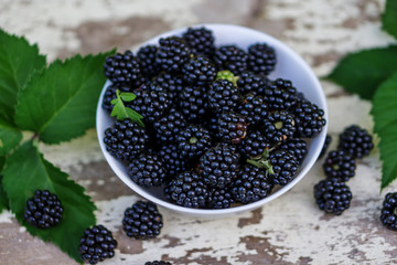 Close up of a cup of ripe blackberries placed on a white rustic table in the garden. Shallow depth of focus. Health concept from nature.