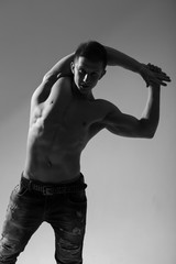 Fototapeta na wymiar Athlete in jeans with a bare torso posing on a gray background. Black and White