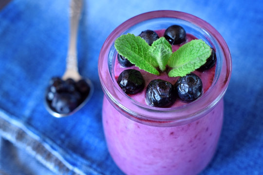 Blueberry smoothie in a glass jar topped with berries and mint on blue background