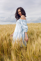 woman in a blue light dress stands in a field with yellow dry ears of wheat in the summer
